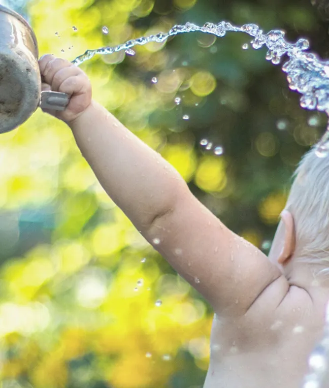 Kind spielt mit Wasser im Garten – Leitmotiv für die Frage, ob Babys spezielles Wasser brauchen.