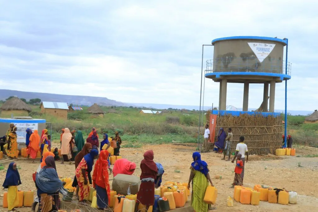 Menschen holen Wasser von einem Wassertank in einer ländlichen Umgebung.