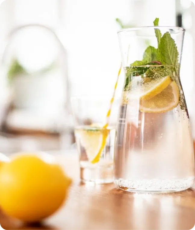 Karaffe mit Zitronenscheiben und Minze auf einem Esstisch aus Holz.