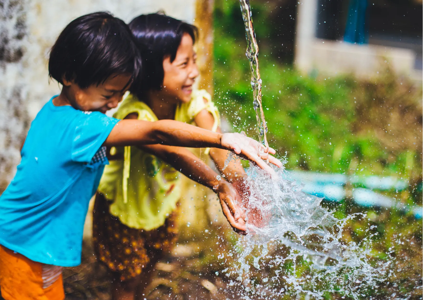 Zwei Kinder spielen lachend mit fließendem Wasser aus einem Brunnen