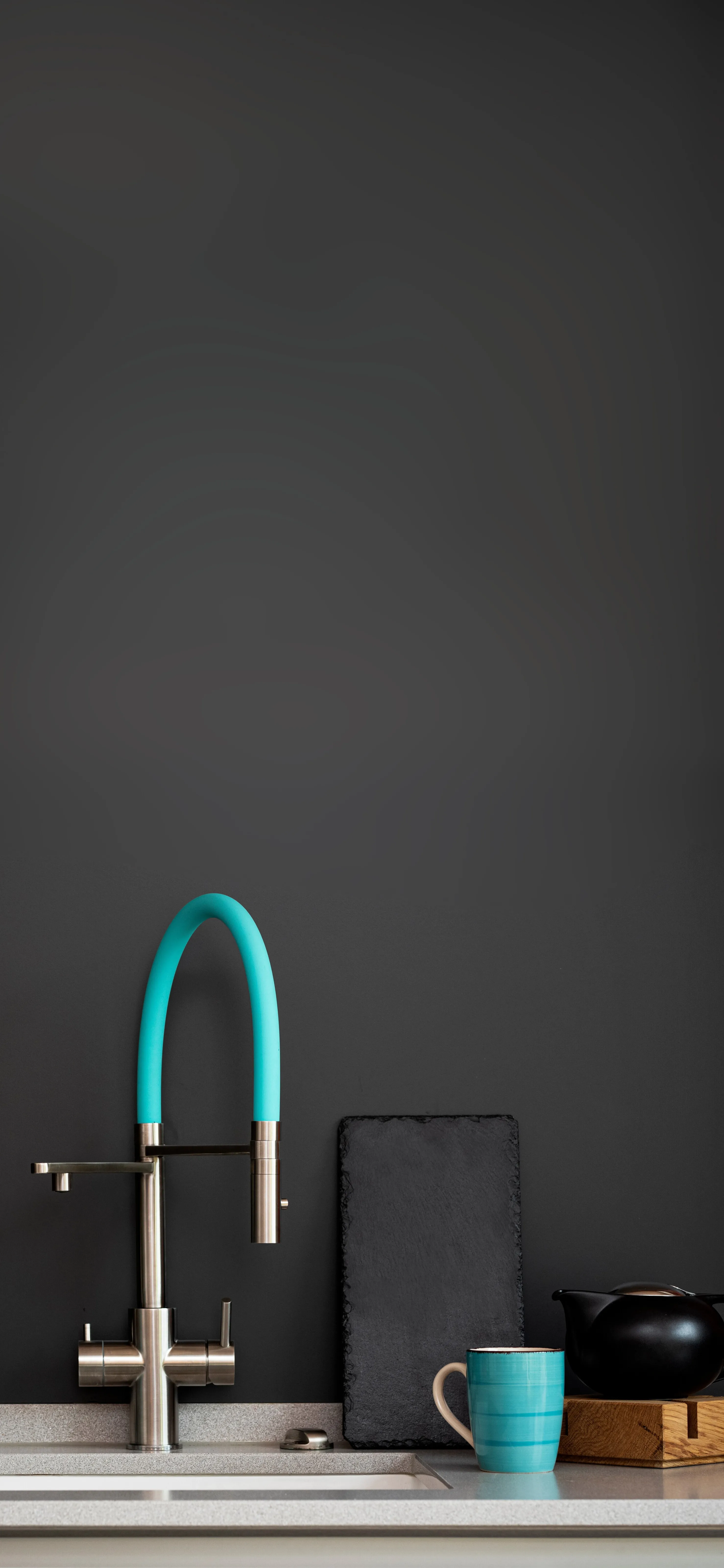 Moderne Küche mit einem Wasserhahn in Türkis, einer schwarzen Platte, einer blauen Tasse und einem Teekessel.
