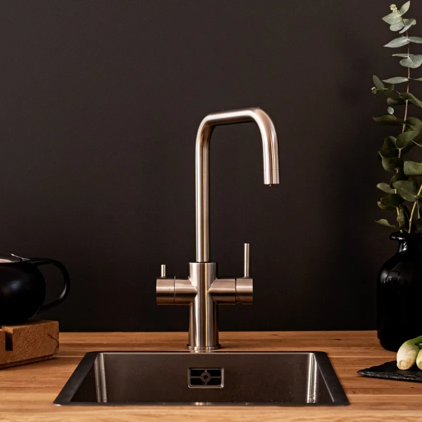 Moderne Küchenarmatur über einem Edelstahlbecken, mit einem schwarzen Hintergrund und einigen Pflanzen im Hintergrund.