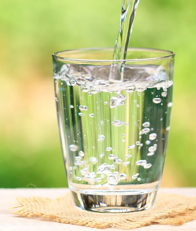 Ein Glas mit sprudelndem Wasser, das auf einem Tisch steht, mit einem unscharfen, grünen Hintergrund.