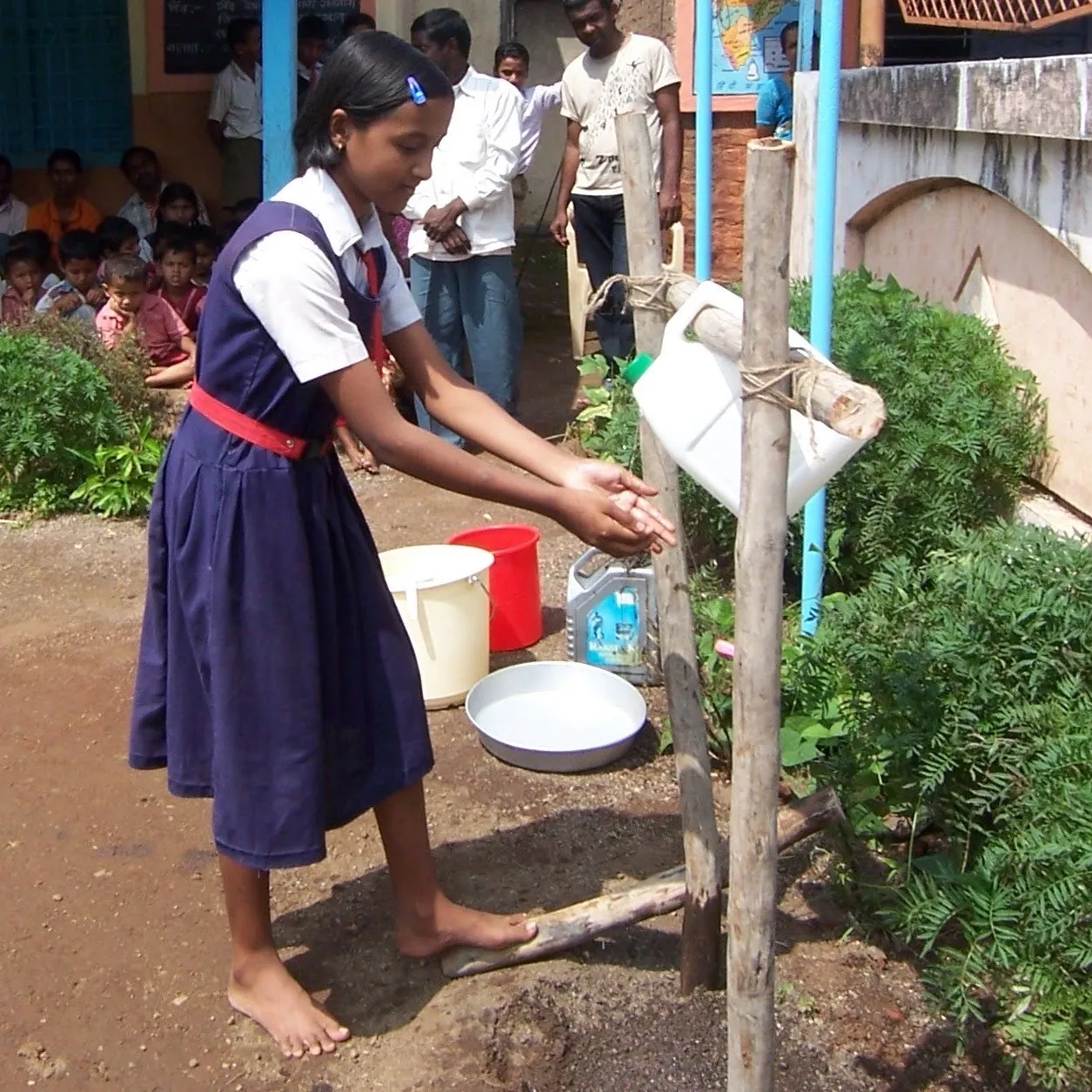Schulkind wäscht sich draußen an einem Tippy Tap die Hände.