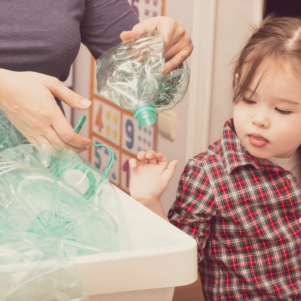 Kind und Erwachsene sortieren gemeinsam leere Plastikflaschen in einem weißen Behälter.