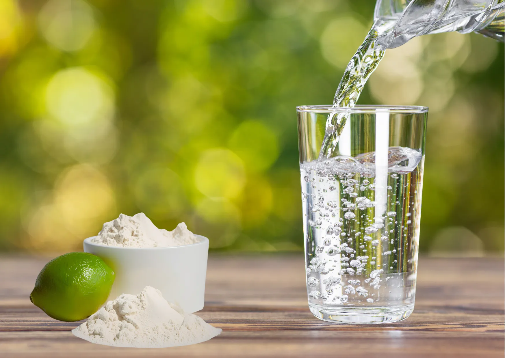 Glas mit sprudelndem Wasser, daneben Mineralpulver und Limette auf Holztisch im Grünen