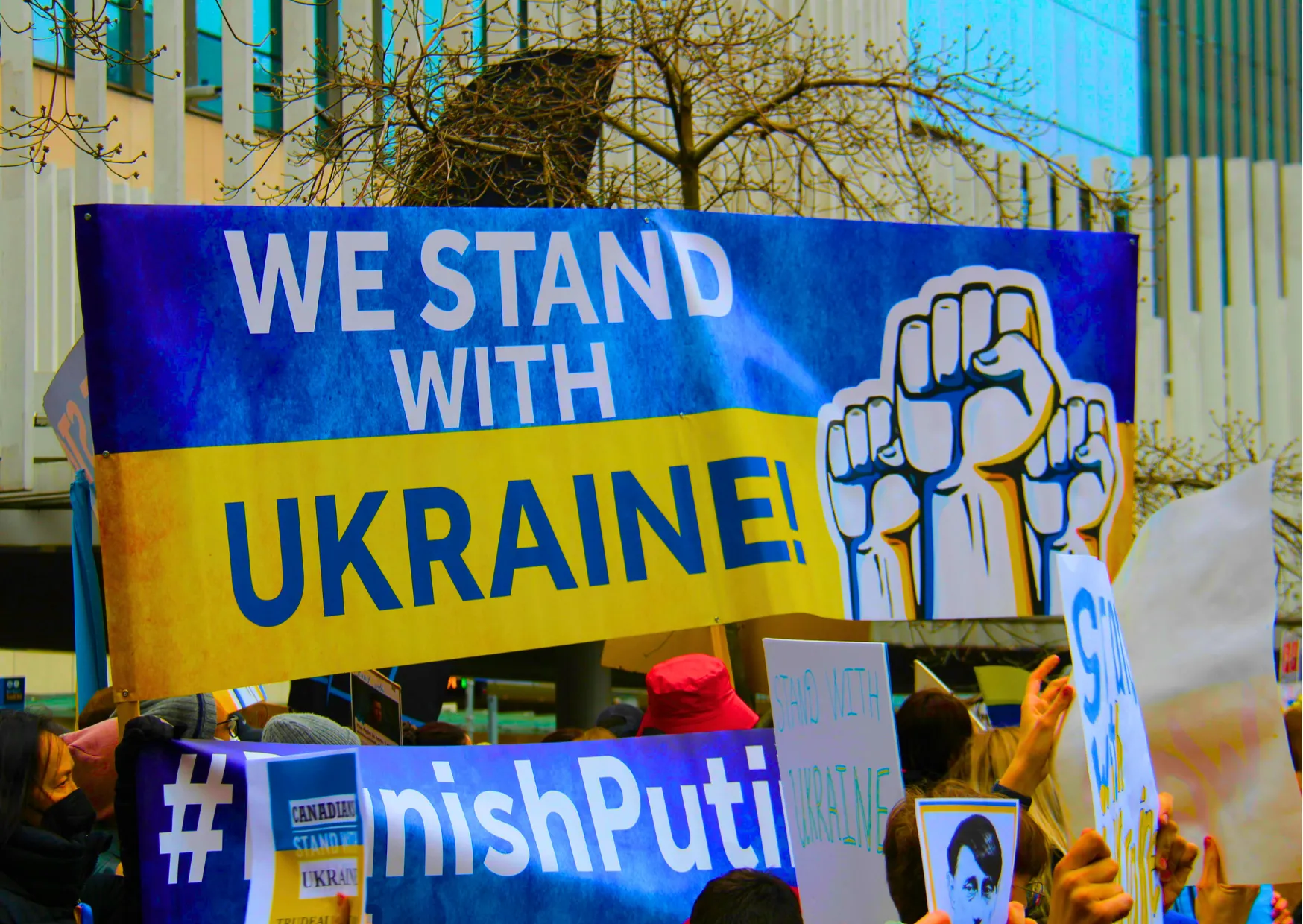 Demonstranten halten ein Banner mit der Aufschrift "WE STAND WITH UKRAINE!" in den Farben der ukrainischen Flagge.