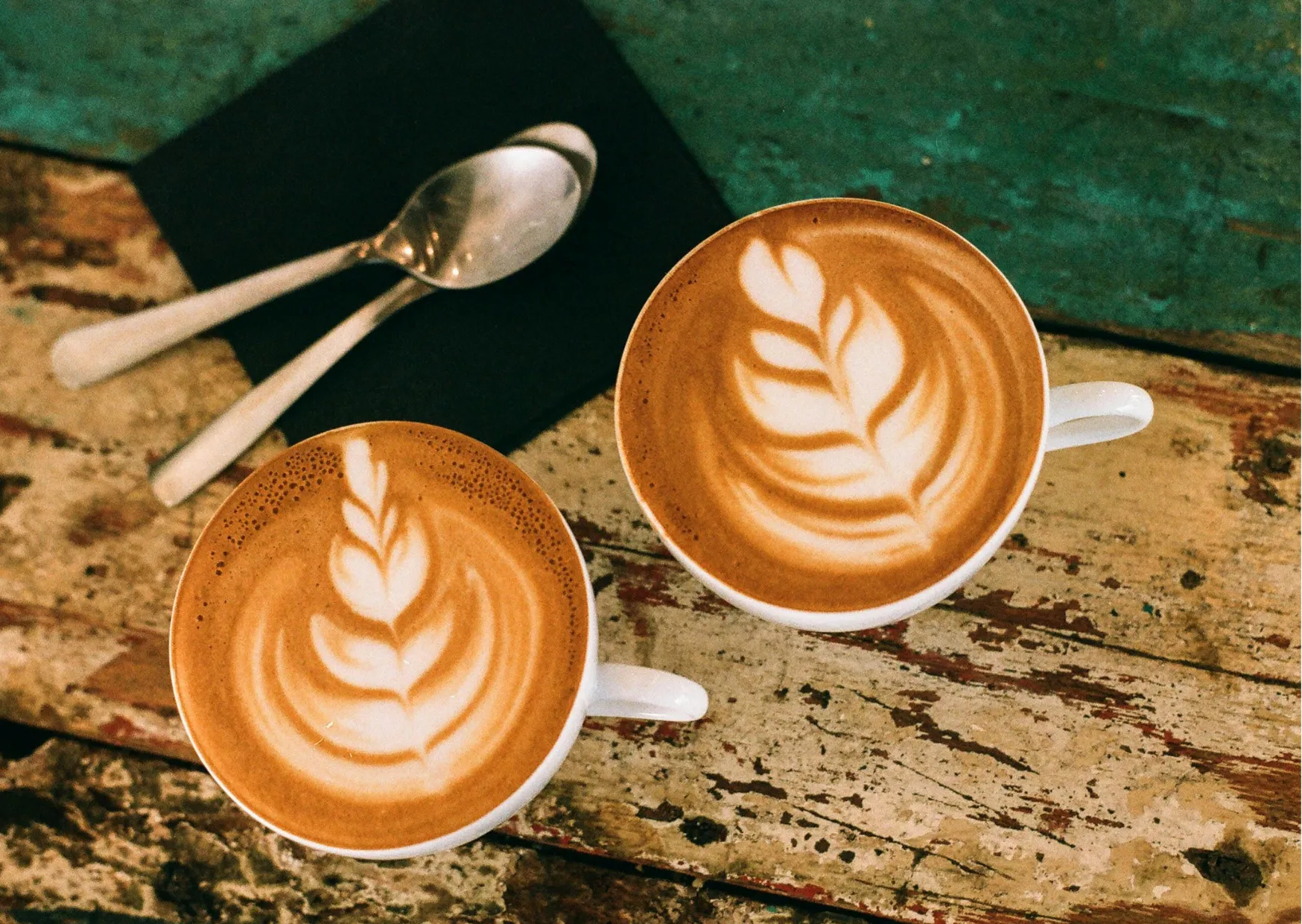 Zwei Tassen Kaffee mit kunstvoller Milchschaum-Dekoration auf einem rustikalen Tisch.