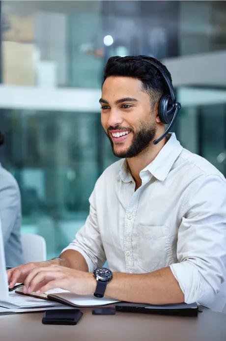 Junger Mann mit Headset, der an einem Laptop arbeitet und lächelt.