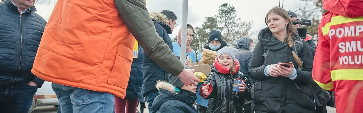 Eine Gruppe von Menschen, darunter ein Kind, das Essen erhält. Freiwillige verteilen Lebensmittel.