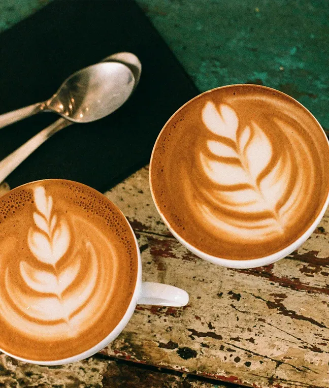 Kaffeetassen mit kunstvoller Milchaufschäumung, daneben Löffel auf Serviette