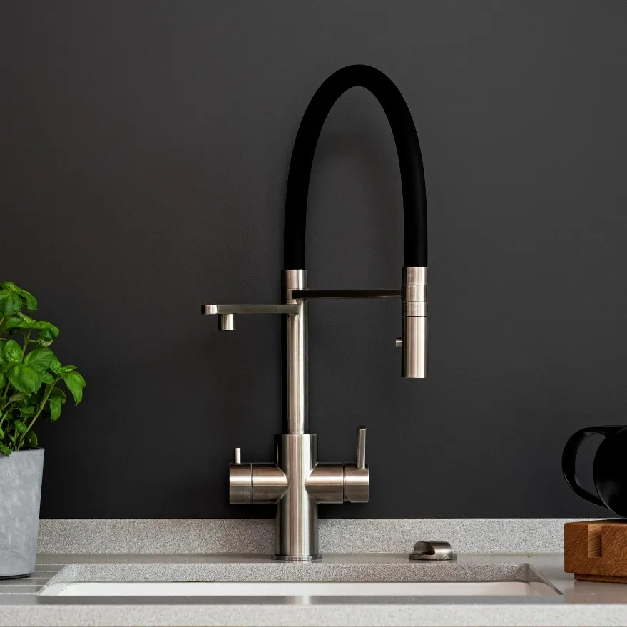 Moderne Küchenarmatur mit schwarzem Schlauch, Edelstahlkörper und Pflanze im Topf auf einer grauen Arbeitsfläche.