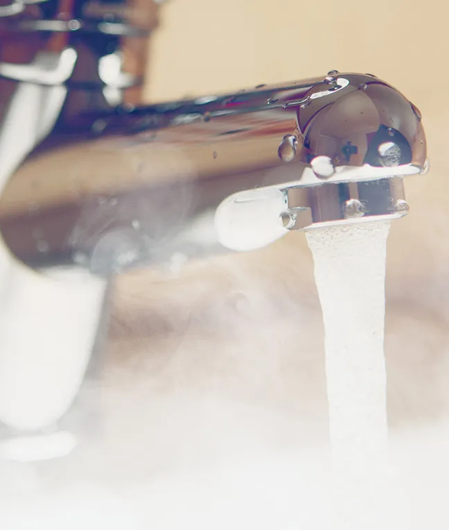Wasser tropft aus einem glänzenden Wasserhahn, umgeben von Dampf.